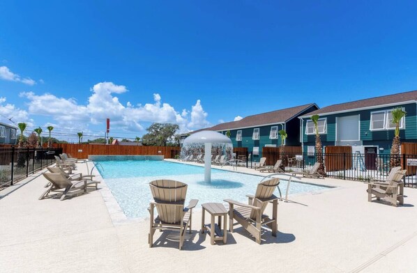 A swimming pool with lounge chairs and a water feature, surrounded by a wooden fence and a building with a blue exterior.