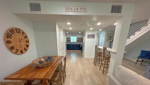 A dining area with a wooden table and chairs, a clock on the wall, and a sign above reading "SEA LA VIE".