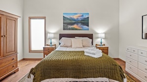 A bedroom with a bed, wooden wardrobe, nightstands, and a painting of a mountain landscape.