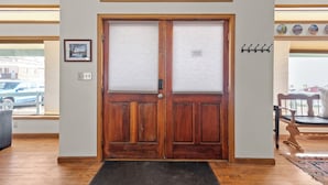 A wooden double door with a doorknob, a doormat, and a wall-mounted coat rack with hooks.