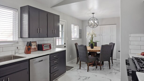 A modern kitchen with dark cabinets, a dishwasher, and a dining area with a wooden table and chairs. - Unwind in this newly updated 4-bedroom home (Laramie)