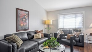 A living room with a black leather sofa, a glass coffee table, and a framed movie poster on the wall. - Unwind in this newly updated 4-bedroom home (Laramie)