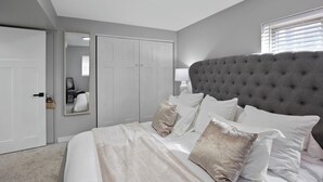 A bedroom with a large bed, grey walls, a grey tufted headboard, and a white door. - Unwind in this newly updated 4-bedroom home (Laramie)