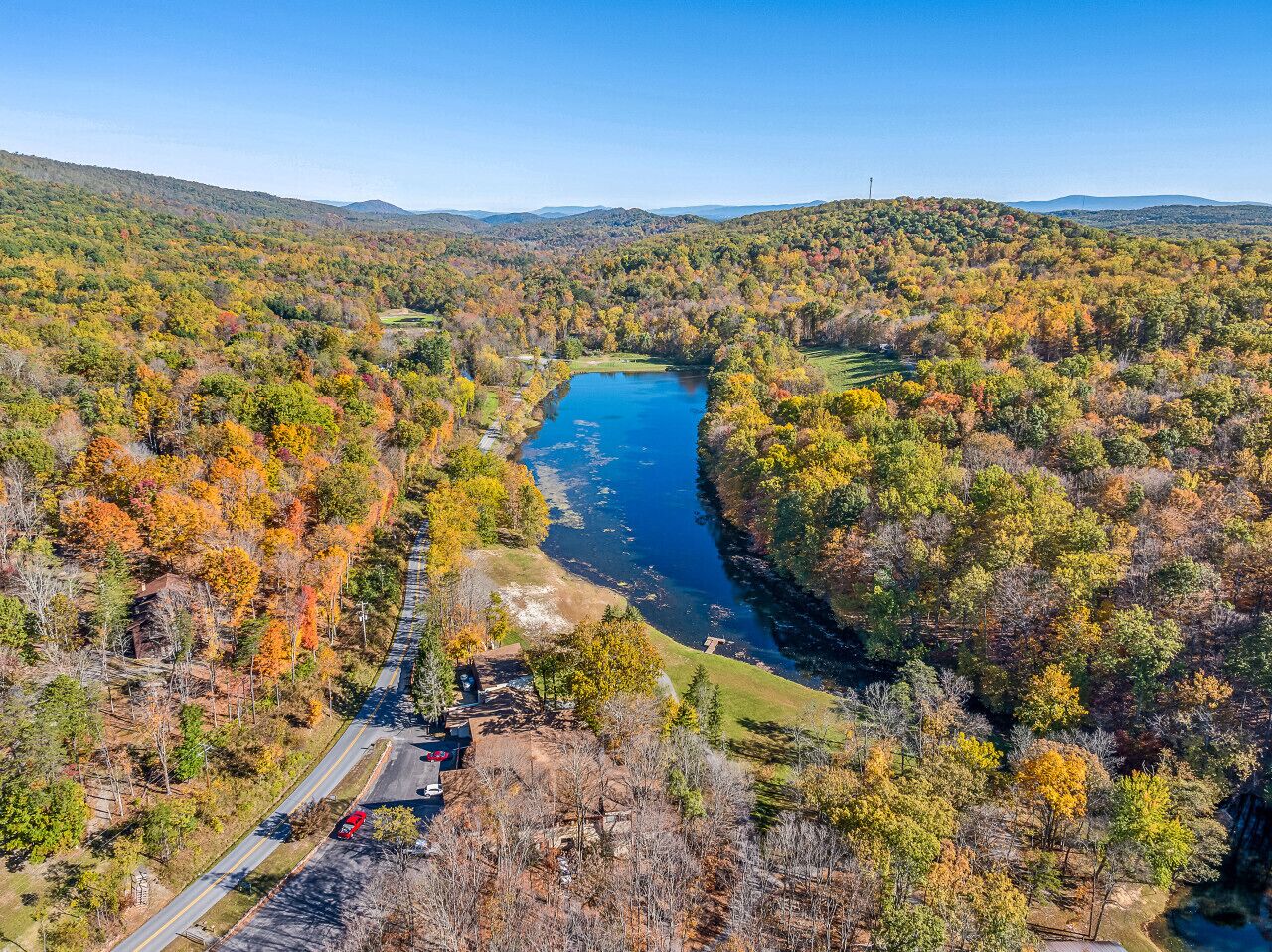 An aerial view of a river surrounded by autumn-colored trees and a road with vehicles.
