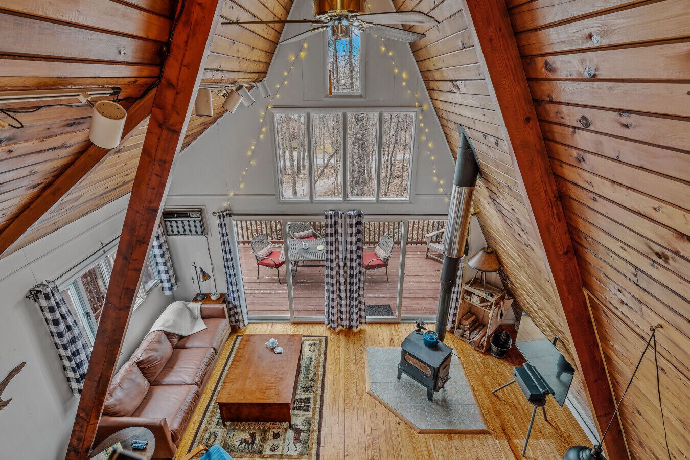A cozy cabin interior with a loft bedroom, a fireplace, and a deck with outdoor seating.