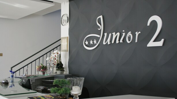 A reception desk with a sign reading "Junior 2" and a clock on the wall. - Hotel Junior 2 (Kraków)
