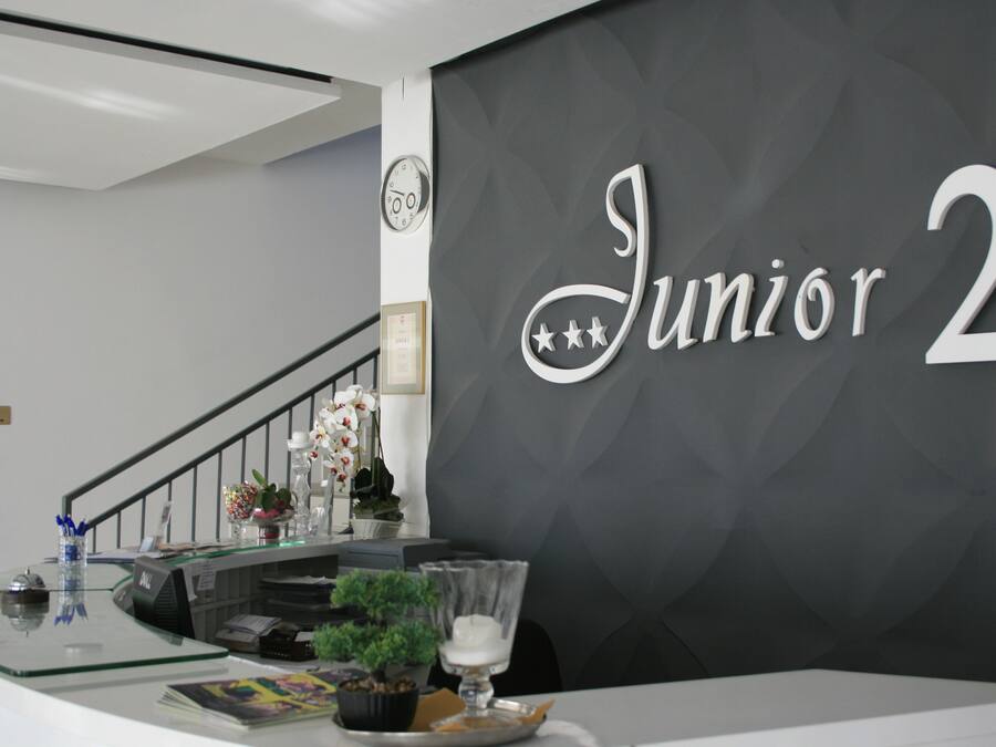 Een receptiebalie met een bord waarop 'Junior 2' staat en een klok aan de muur.