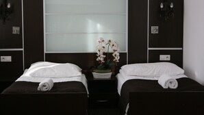 A hotel room with two single beds, a large window with frosted glass, a small table with a vase of flowers, and a wall-mounted light fixture. - Hotel Junior 2 (Kraków)