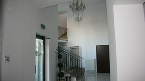 A spacious hallway with a staircase leading to an upper floor, a chandelier, and a door at the end. - Hotel Junior 2 (Kraków)