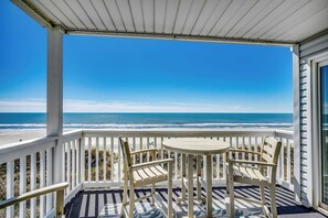 A covered balcony with a view of the ocean, featuring two wooden chairs and a small round table.