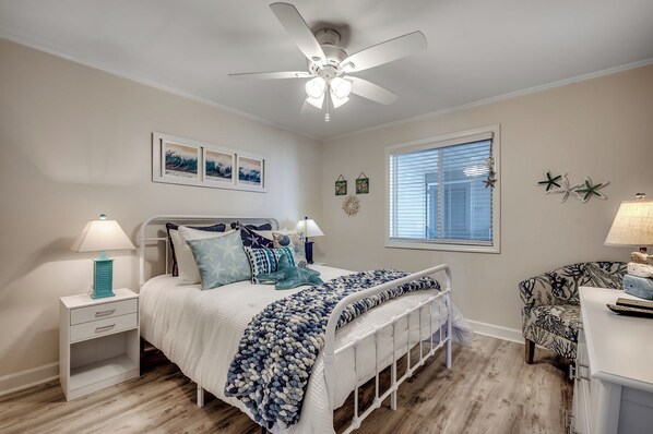 A bedroom with a bed, nightstands, a desk, a ceiling fan, and a window with blinds.
