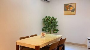Un comedor con una mesa, sillas, un equipo de aire acondicionado, una planta en la pared y un candelabro.