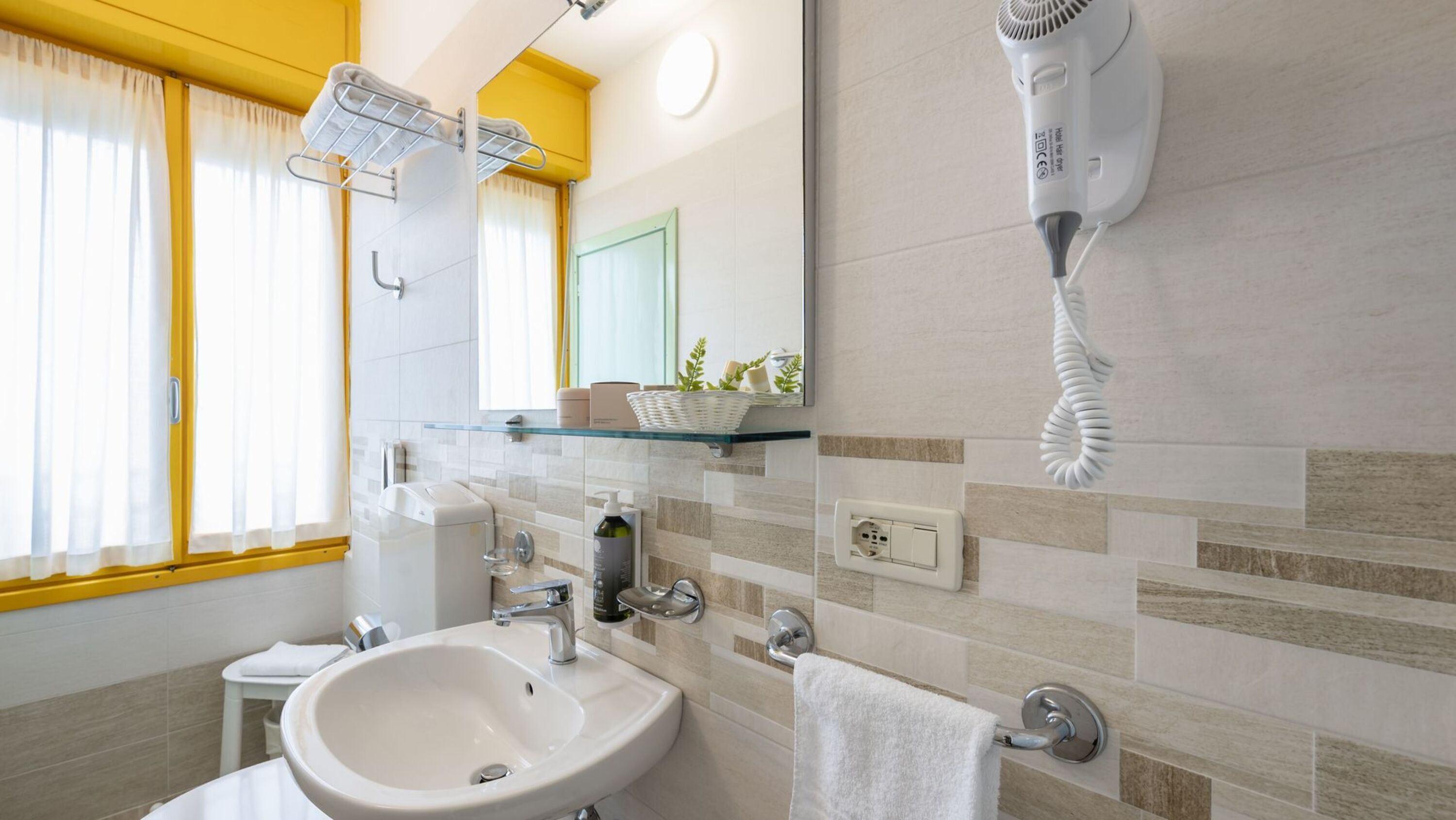 Une salle de bain équipée d’un lavabo, d’un miroir, d’un porte-serviettes et d’un sèche-cheveux.