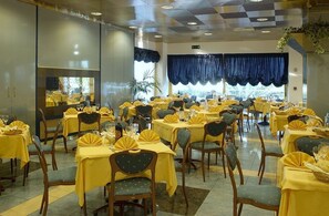 Une salle à manger avec plusieurs tables dressées, ornées de nappes jaunes et de housses de chaise assorties.