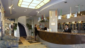 A hotel lobby with a reception desk, a staircase, and a seating area.