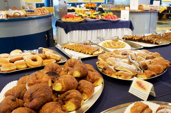 Un bufé con diversas opciones de panadería, incluyendo croissants, pasteles y gofres.