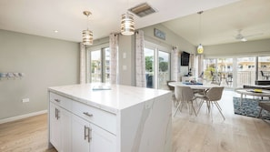 A modern kitchen with a marble island, pendant lights, and a dining area with chairs and a table. - Port Largo Villas Escape 5A (Key Largo)