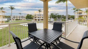 A balcony with a table and chairs, overlooking a grassy area and buildings.
