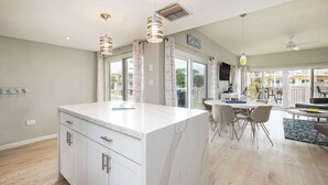 A modern kitchen with a marble island, pendant lights, and a dining area with chairs and a table. - Port Largo Villas Escape 5A (Key Largo)