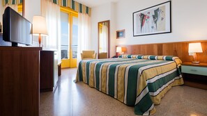 Una habitación de hotel con cama, escritorio, televisor y un cuadro en la pared.