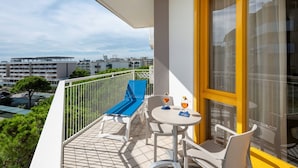 A balcony with a blue chair, a table with a glass of drink, and a view of buildings in the distance. - Seaside escape for perfect vacations in Bibione (Bibione)