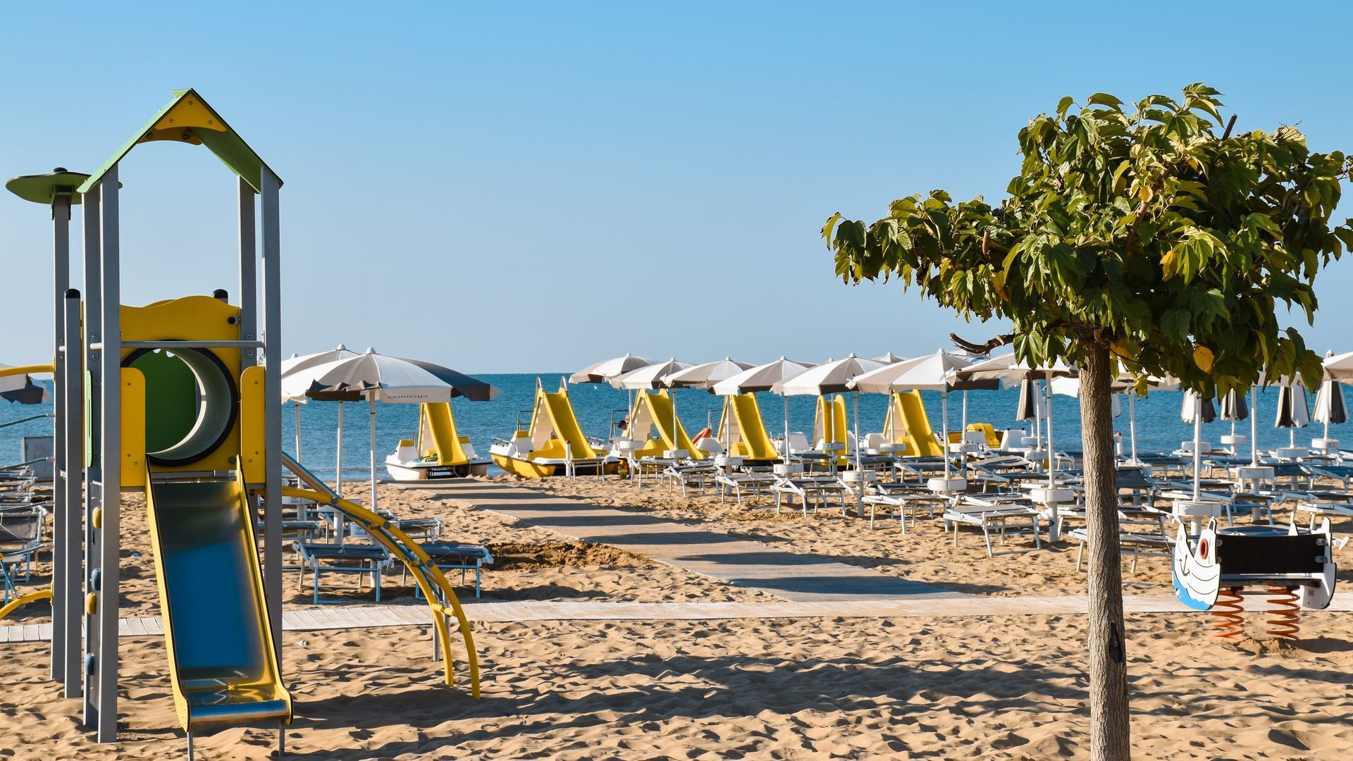 Une plage avec des transats, des parasols et une aire de jeux.
