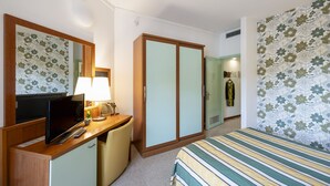 Ein Hotelzimmer mit einem Bett, einem Schreibtisch mit Lampe, einem Fernseher und einem Kleiderschrank.