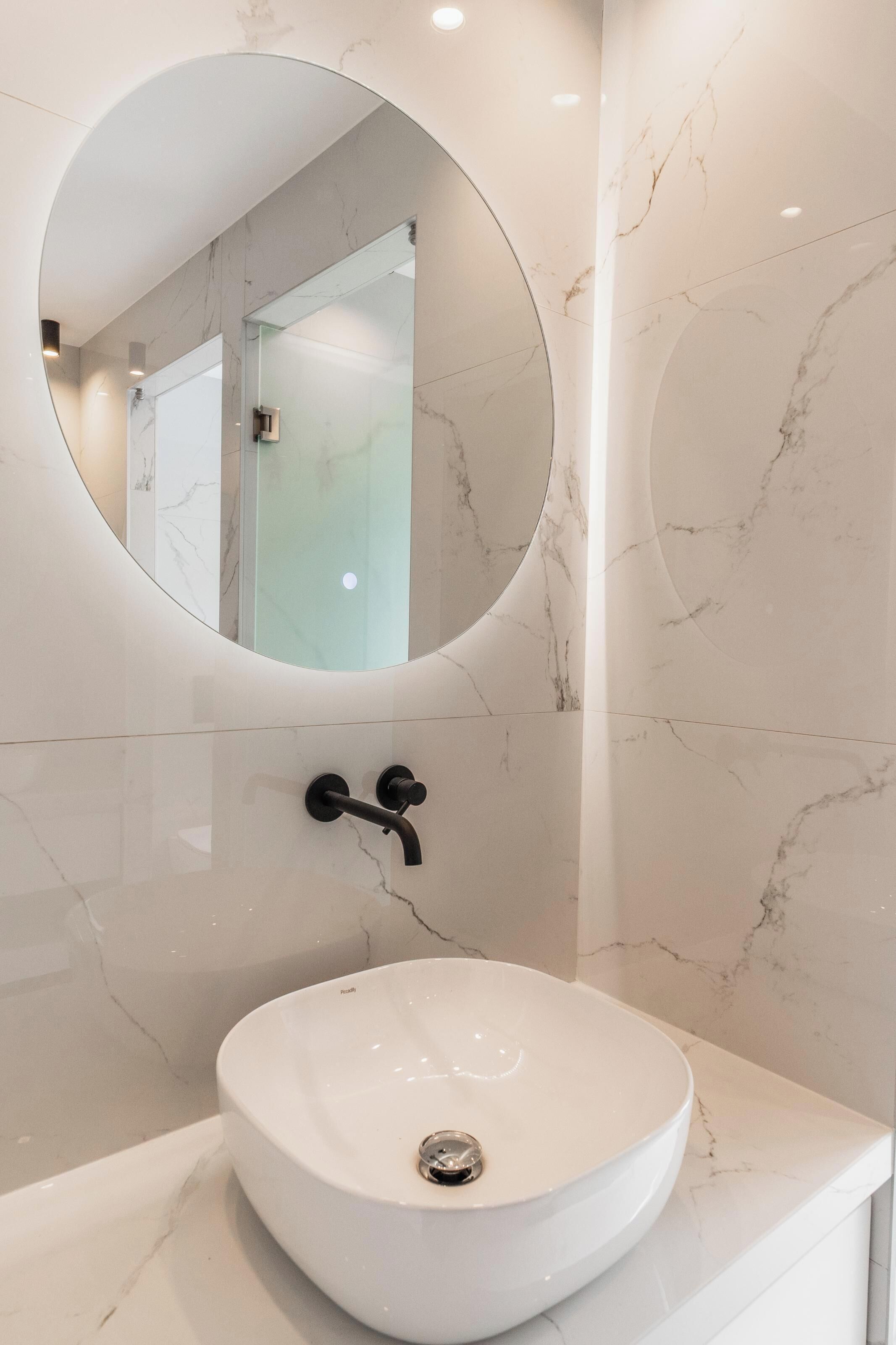 A modern bathroom with a round mirror, a white marble sink, and a sleek faucet.