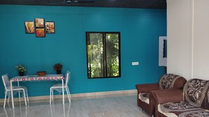 A living room with a teal wall, a brown sofa, a dining table with chairs, and a window with a view of trees.