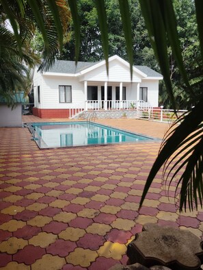 A house with a swimming pool, surrounded by a tiled patio and greenery.