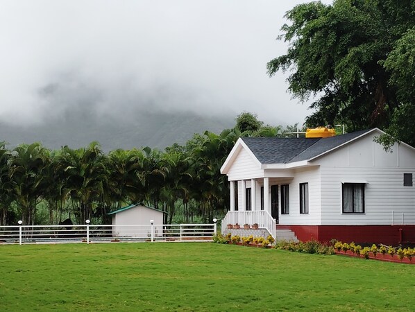 A white house with a red base, surrounded by a white fence and lush greenery.