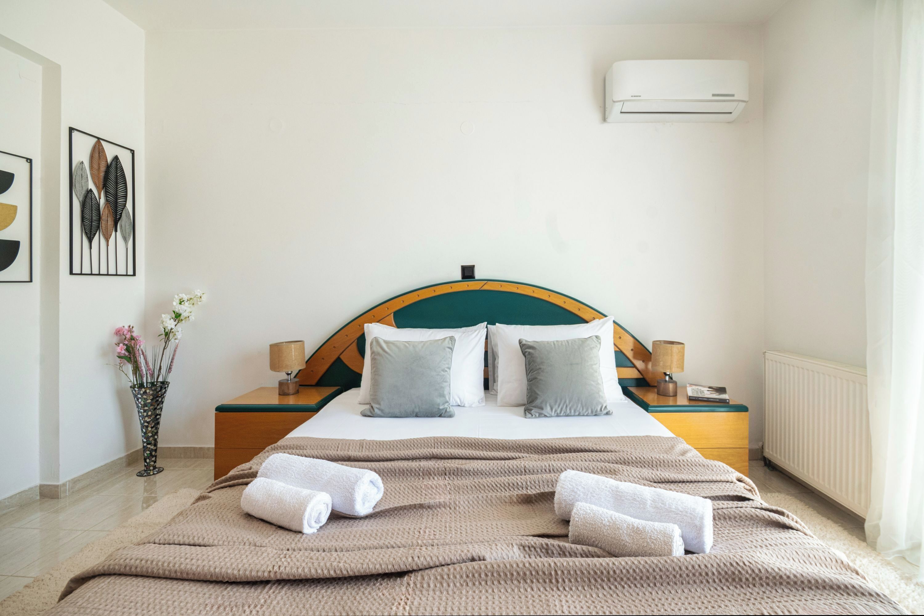 Una camera d'albergo con un letto, comodini, un vaso con fiori e un condizionatore d'aria.