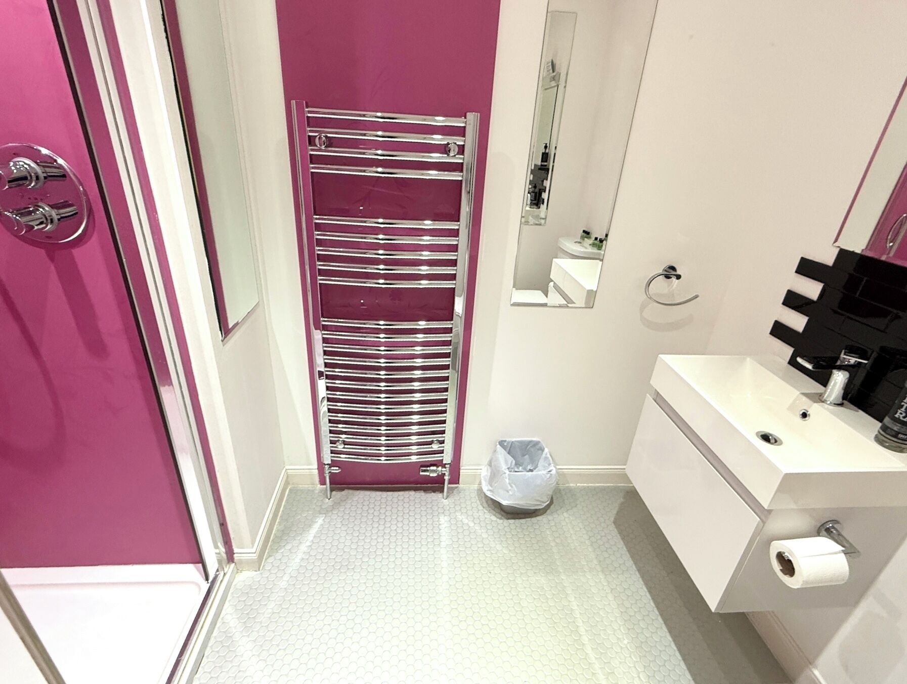 A bathroom with a pink wall, a chrome towel rack, a white sink, and a mirror.