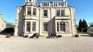 A historic stone building with multiple windows, a corner turret, and a gravel driveway. - Seabank House Hotel (Nairn)