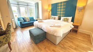 A modern hotel room with a large bed, a sofa, and a view of greenery outside. - Seabank House Hotel (Nairn)