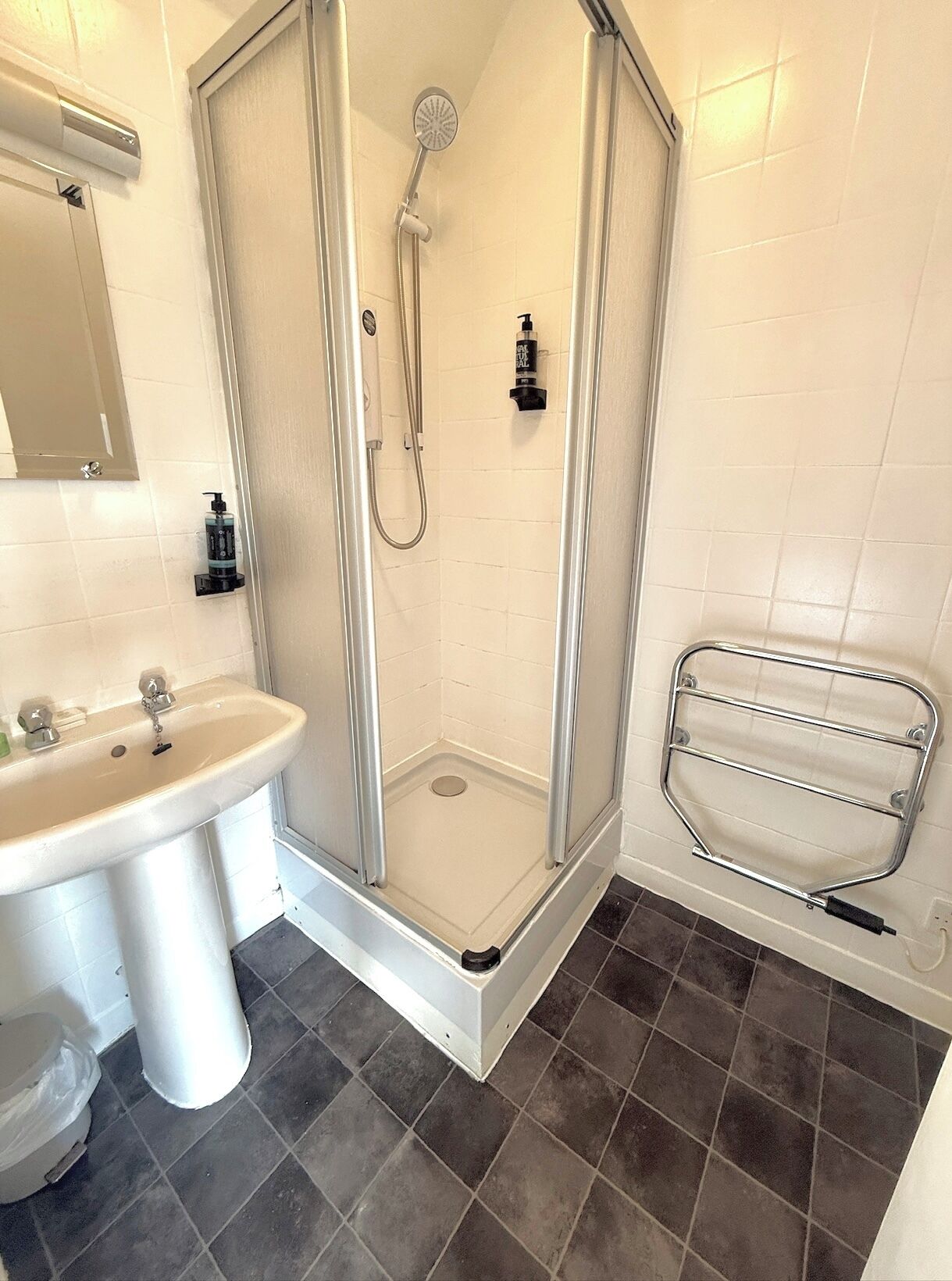 A bathroom with a shower enclosure, a sink, and a towel rack.