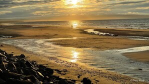A beach with the sun setting over the horizon, creating a reflection on the wet sand. - Seabank House Hotel (Nairn)