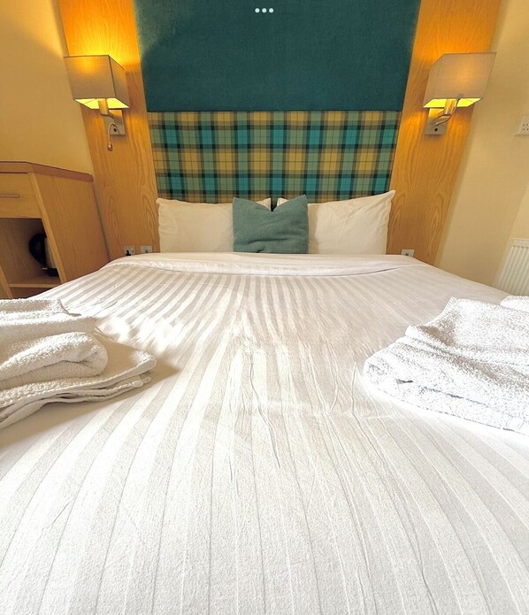 Una habitación de hotel con una cama grande, cabecera de cuadros y dos lámparas fijadas a la pared.
