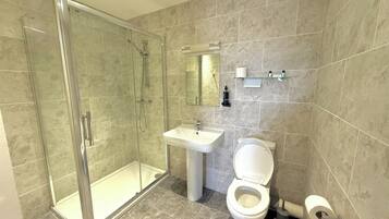 Un baño moderno con cabina de ducha de vidrio, lavamanos pedestal y retrete.