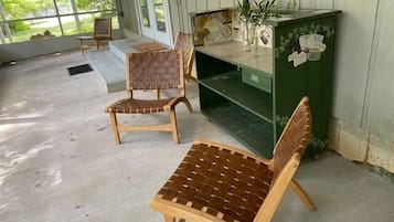 Une véranda couverte avec deux fauteuils en osier et un meuble vert contenant des objets décoratifs.