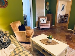En stue med en ternet sofa, en beige lænestol, et hvidt sofabord med en plante og en pude med Florida-motiver på en stol.