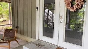 Un porche avec un banc en bois, une porte ornée d’une guirlande et un paillasson.