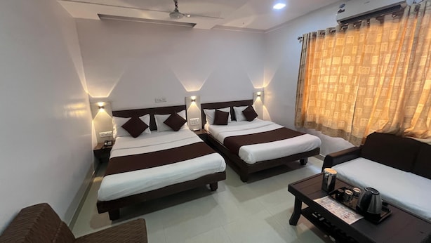 A hotel room with two beds, a sofa, a coffee table, and an air conditioning unit. - Hotel Anupam (Mahabaleshwar)