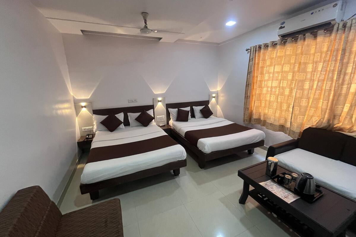 A hotel room with two beds, a sofa, a coffee table, and an air conditioning unit.