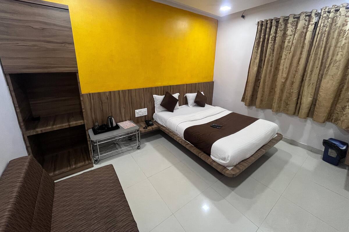 A hotel room with a bed, a nightstand, a wardrobe, a small table, and a curtain.
