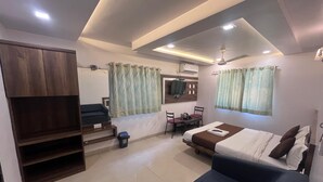 A compact hotel room with a bed, a sofa, a TV, a desk with chairs, and a staircase. - Hotel Anupam (Mahabaleshwar)