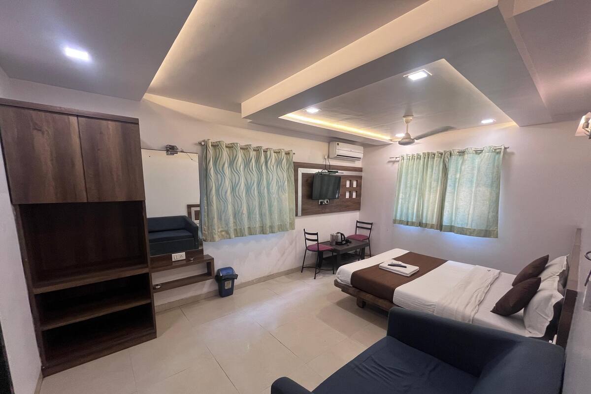 A compact hotel room with a bed, a sofa, a TV, a desk with chairs, and a staircase.