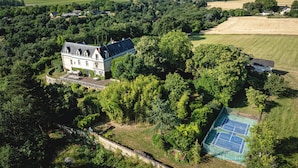 An aerial view of a large estate with a prominent house surrounded by dense trees and fields. - Castle near Saumur with stunning Loire view, large nature chateau with tennis (Gennes-Val-de-Loire)