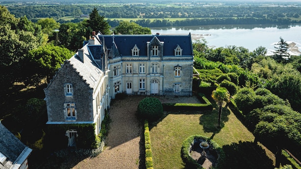 A large, historic building with a symmetrical facade, a central courtyard, and a view of a lake. - Castle near Saumur with stunning Loire view, large nature chateau with tennis (Gennes-Val-de-Loire)