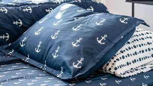Een bed met marineblauwe beddengoed met ankerprint, een wit metalen frame en een blauw gordijn met patroon.